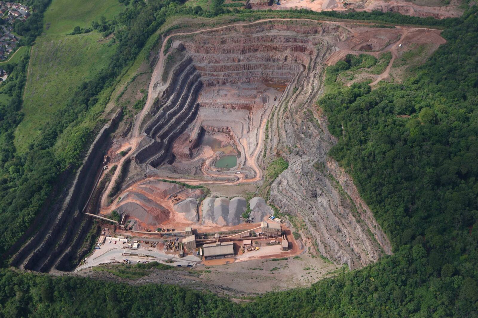 Aerial view of Taffs Well Quarry, showing the stepped quarry faces, stockpiles and processing plant surrounded by woodland