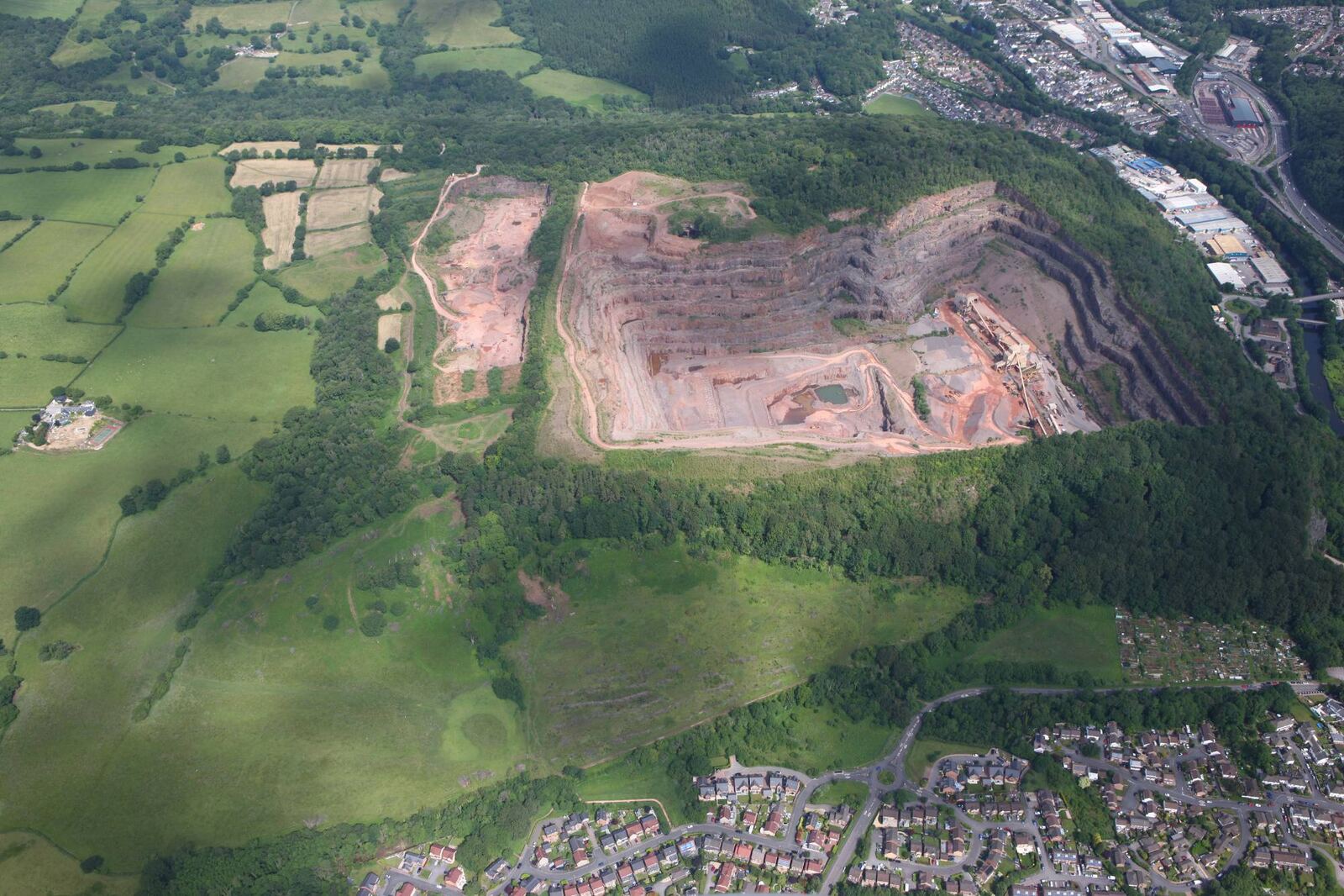 Wide aerial view of Taffs Well Quarry in its setting, with farmland, woodland and nearby housing